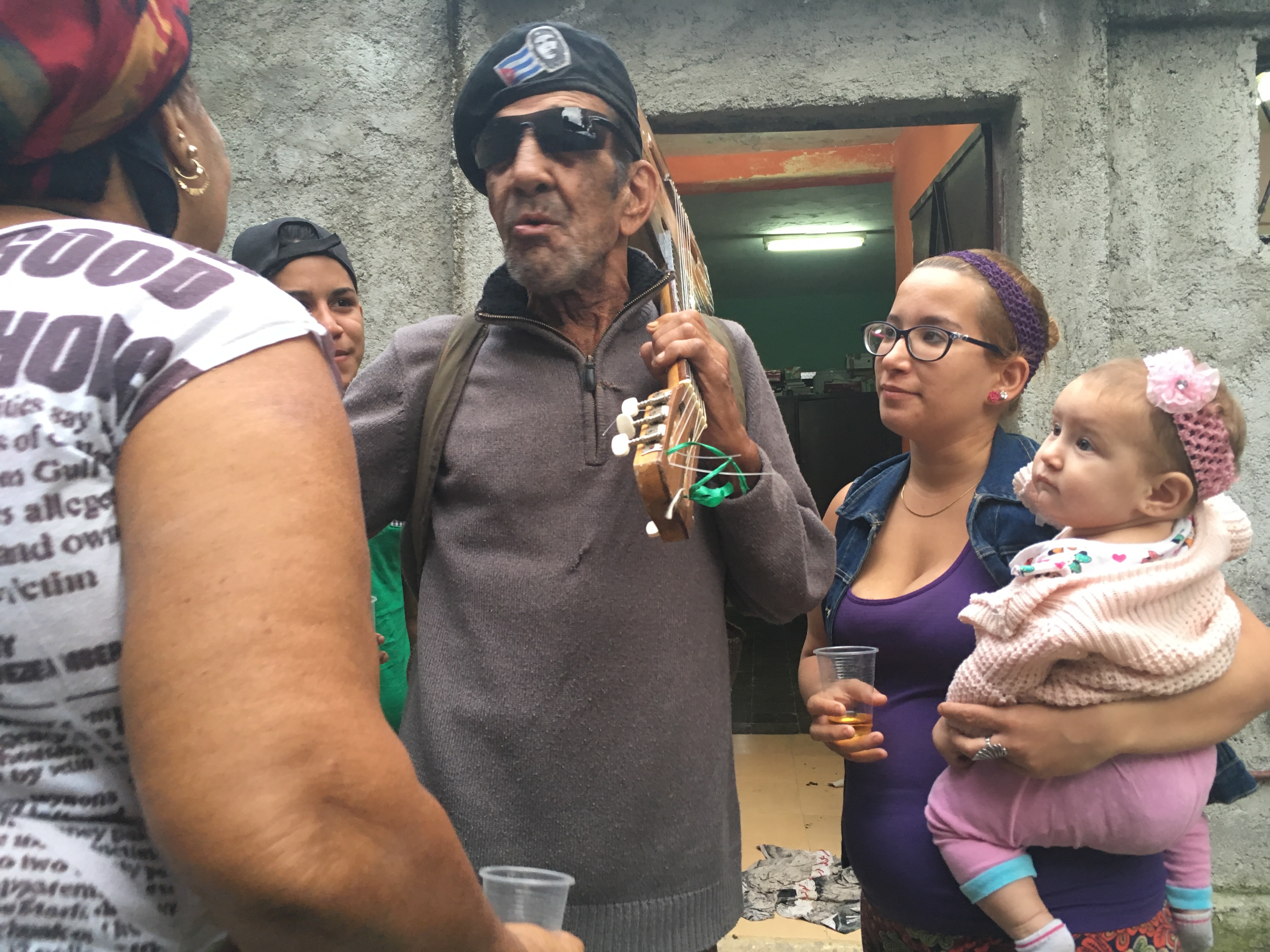 Papi wearing a Che Guevara beret, guitar slung over his shoulder, singing among family.