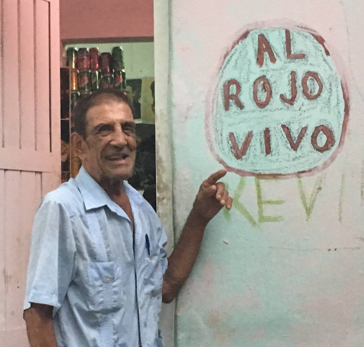 Papi señalando el grafiti 'AL ROJO VIVO' en la pared junto a su puerta.