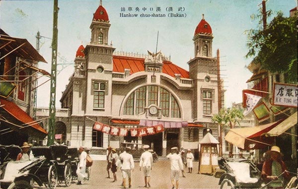 A colorized postcard of Hankow Station: a two-towered building with red domes and a large arched window, and rickshaws and men in white clothes in the square in front