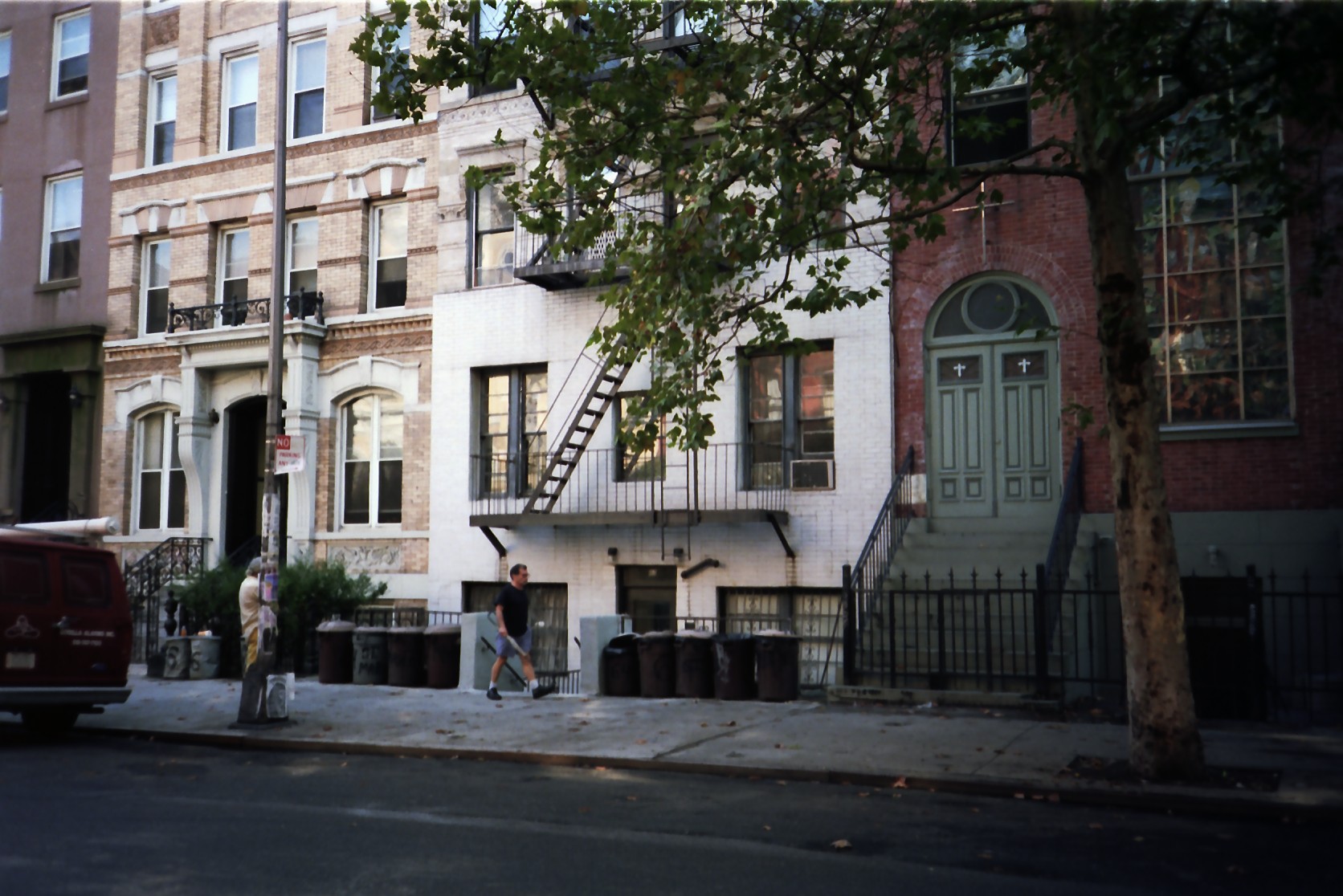 Una hilera de edificios en el East Village, Nueva York: un edificio de apartamentos blanco con escalera de incendios, junto a una iglesia con puertas verdes